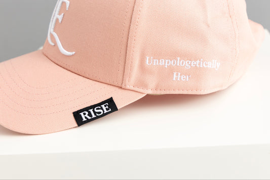 Pink cap with 'RISE' and 'Unapologetically Her' text on a light background